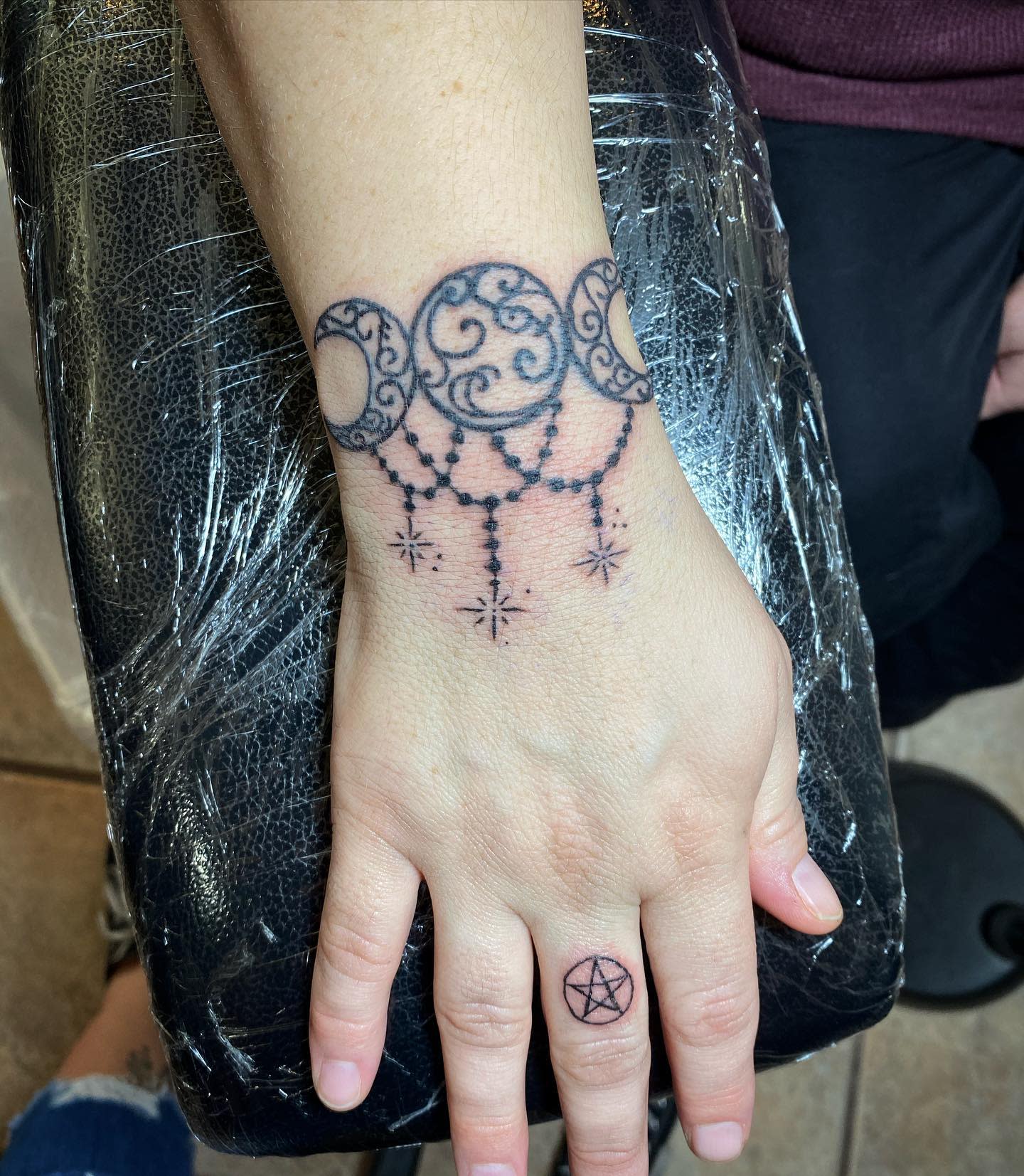Hand with moon phase and stars tattoo on the wrist; pentagram tattoo on the finger